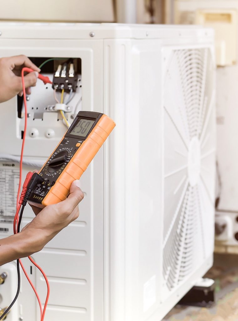 Air repair mechanic using measuring equipment for filling industrial factory air conditioners and checking maintenance outdoor air compressor unit.